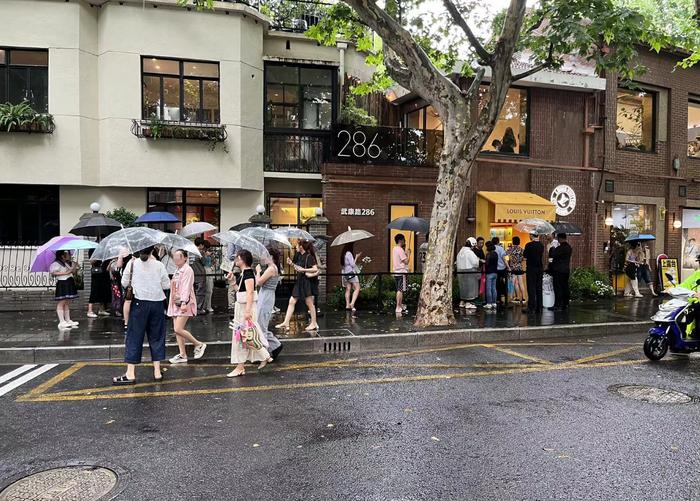 ↑门店外，人们在雨中排起了队