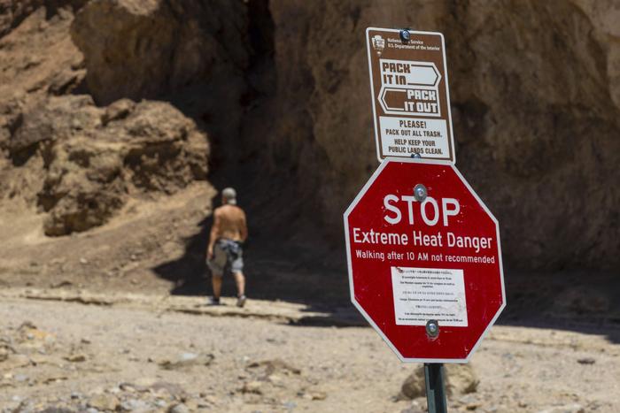 当地时间2023年7月11日，美国加州死亡谷国家公园，一名徒步旅行者经过一个警告极端高温的告示牌。图/视觉中国