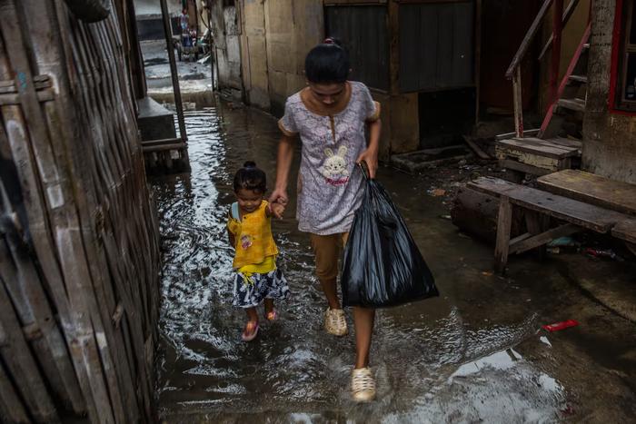 ▲雅加达北部涨潮期间，母亲和孩子走在被洪水淹没的街道上