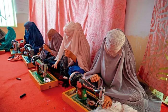 阿富汗坎大哈，身穿罩袍的妇女在裁缝车间缝制衣服。